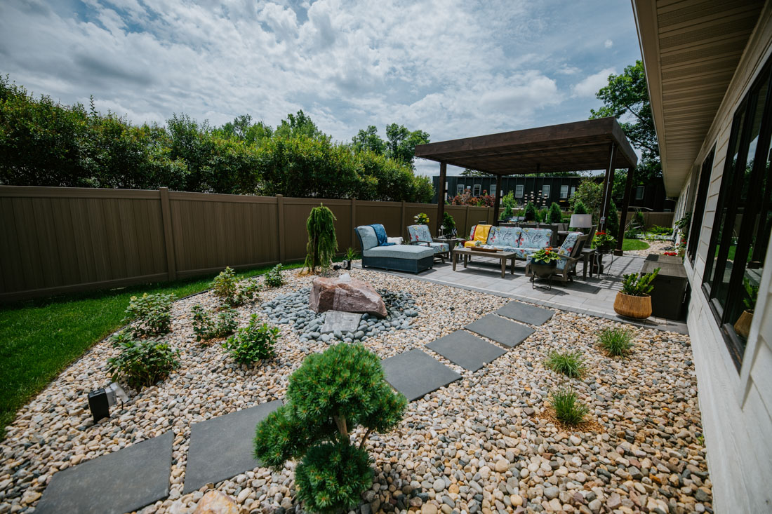 wideview of a backyard with a patio, pergola, and plant beds