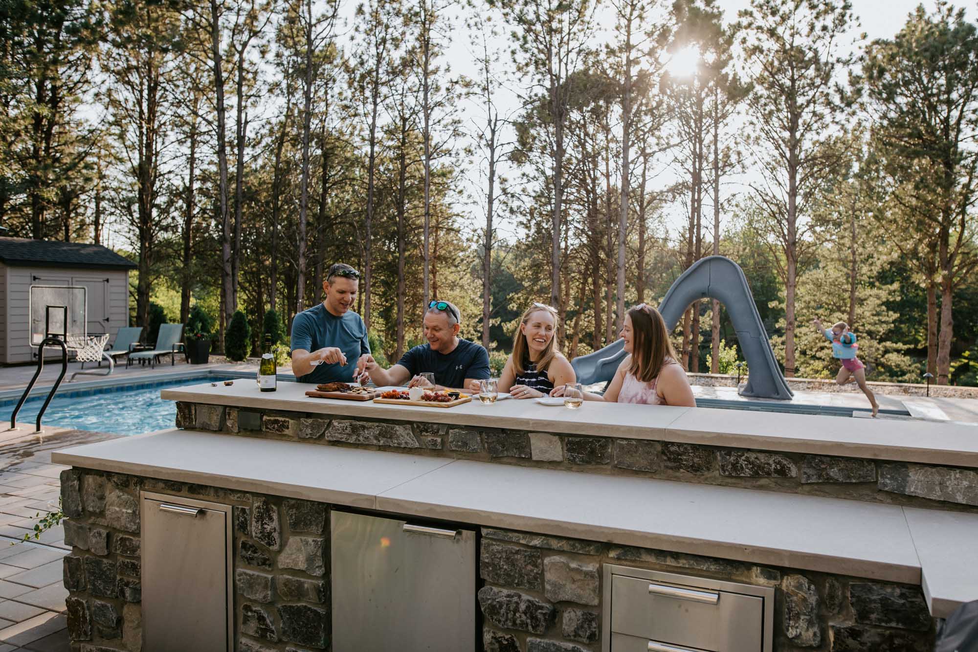 adults enjoying their outdoor kitchen with pool in the background