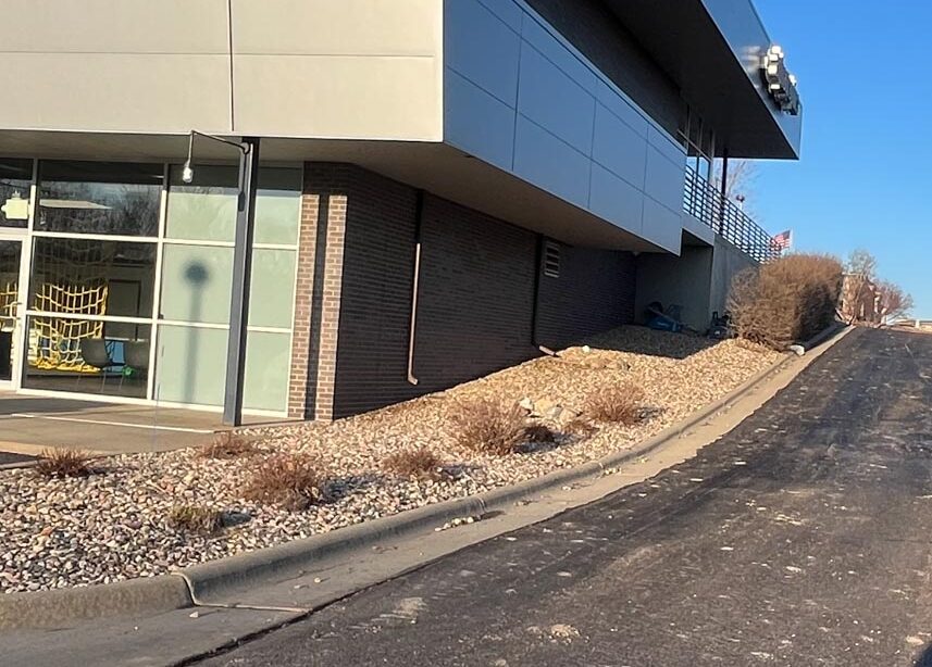 Side of a building with old rock bed and overgrown plant material