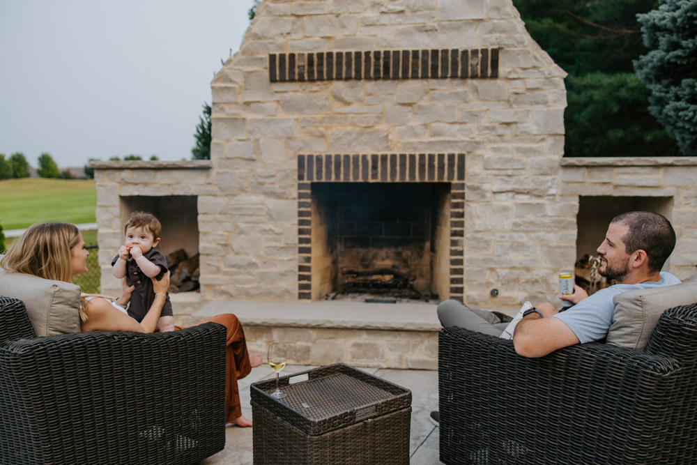 a family of three enjoys an evening in front of a custom masonry outdoor fireplace