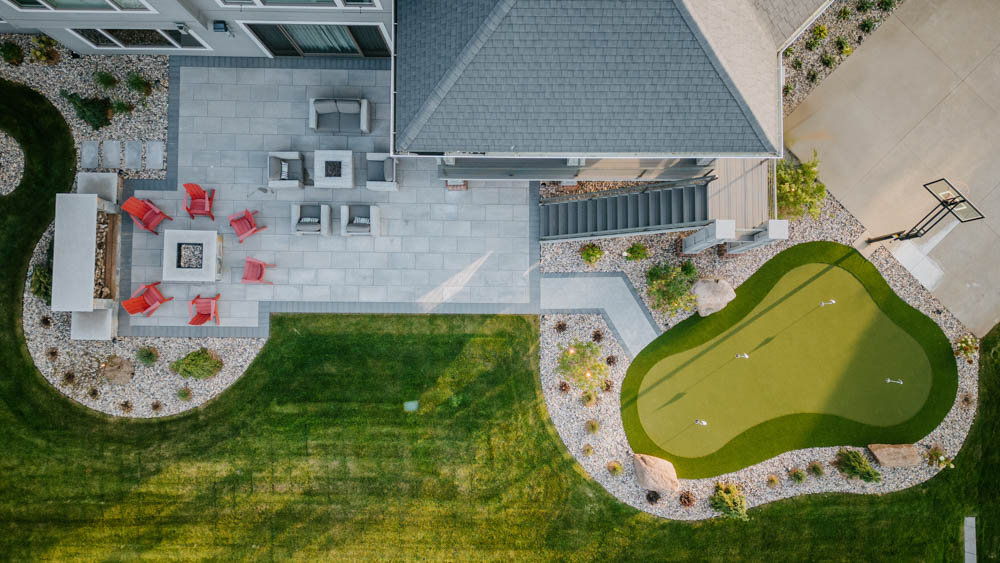 aerial view of backyard landscaping with a patio, fire pit, and putting green